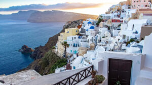 Houses on a cliffside of the island of Santorini with the Aegean sea and a volcanic mountain in the background