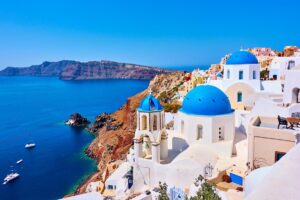 White buildings of Santorini in the foreground with Aegean sea and volcanic island in the background.