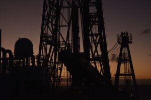Silhouette of the JOIDES Resolution derrick against a dark purple sunset.